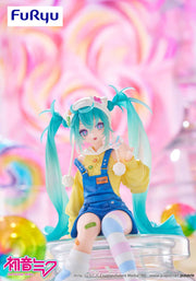 Colorful figurine of Hatsune Miku with teal hair and a yellow outfit, sitting with mismatched knee high socks and holding a pastel colored lollipop.