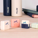 Collection of Milan erasers in plastic cases on a wooden surface with notebooks in the background.