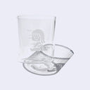 Small clear glass cup with a cartoon graphic on the front of a small girl sitting on the ground and smiling.