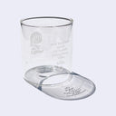 Small clear glass cup with a cartoon graphic on the front of a small girl sitting on the ground and smiling.