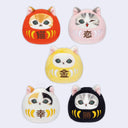 Five cat-shaped daruma plushies with different color schemes and designs on a white background