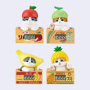 4 small figurines of cats popping up out of a fruit cartoon for varying fruits, each with a small digital clock in the front. Each cat wears a fruit shaped cap matching their box, such as: apple, melon, banana and pineapple.