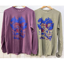 Two long-sleeve shirts, one purple and one green, with a graphic design on a tiled wall background.