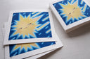 Stack of art prints with an illustration of a yellow starburst shape, it has a facial expression of apathy and star rays behind it, as though falling from a sky.
