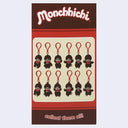 A Monchhichi collectible keychain card featuring 12 mini brown-and-white monkey keychains with red neckties, displayed on a red and brown card with 'Monchhichi' branding at the top and 'collect them all!' at the bottom.
