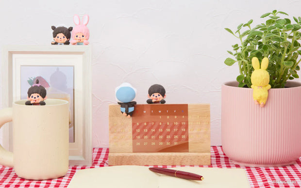 Desk setup with a mug, calendar, plant, and small figurines on a checkered tablecloth.