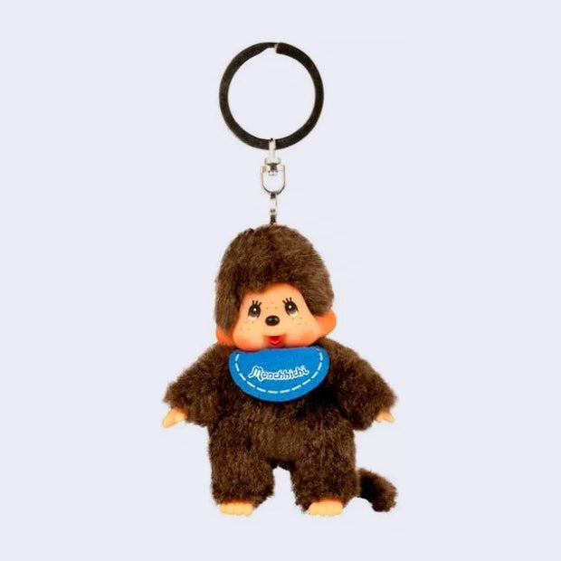 Small plush keychain of a Monchhichi doll,  fluffy monkey plush with a cute face. It wears a blue bib.