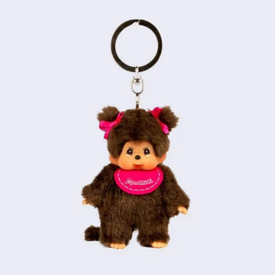 Small plush keychain of a Monchhichi doll, a fluffy monkey plush with a cute face and its hair in pigtails tied by pink bows. It wears a pink bib.