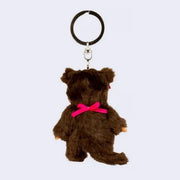 Small plush keychain of a Monchhichi doll, a fluffy monkey plush with a cute face and its hair in pigtails tied by pink bows. It wears a pink bib.