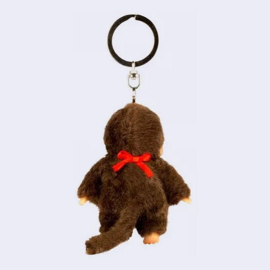 Small plush keychain of a Monchhichi doll, a fluffy monkey plush with a cute face. It wears a red bib. Reverse side.