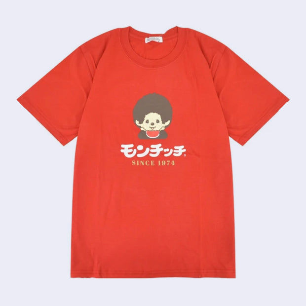 Red t-shirt with a graphic of a Monchhichi, wearing a red bib and holding its head in its hands. Below, is text in Japanese and below that "since 1974" in English.