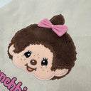 Tote bag with a cartoon Monchhichi girl with a pink bow and 'Monchhichi' branding, close up to show detail.