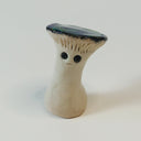 Small sculpture of a mushroom with an anthropomorphic face: a small straight mouth and very large shiny black eyes. The top of the mushroom is flat and shiny. 