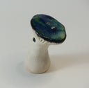 Small sculpture of a mushroom with an anthropomorphic face: a small straight mouth and very large shiny black eyes. The top of the mushroom is flat and shiny. 