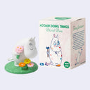 Blind box figure of Moomin leaning over a grassy area and smelling flowers.