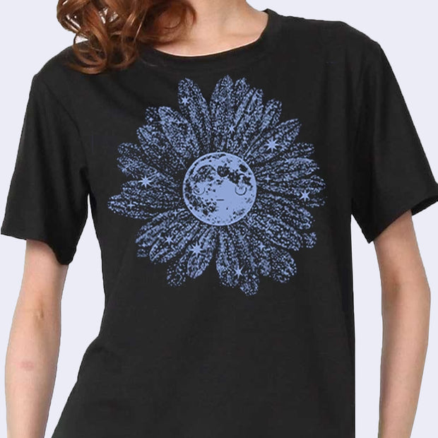 Black shirt with blue lavender colored moon with many starry patterned flower petals coming out of it. The moon has a simple closed eye face. 