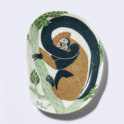 Decorative plate shaped like a slightly distorted oval with a monkey design and floral elements, in earthy tones of green, brown and dark teal. 