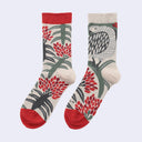 A pair of crew socks with a botanical and bird pattern, featuring red flowers, green leaves, and a gray-and-white bird on a light beige background, with solid red heels, toes, and cuffs.