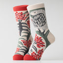 A pair of crew socks with a detailed knit pattern featuring a gray and white owl, red flowers, and green leaves on a cream background, with solid red toes and heels.