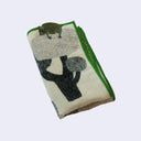 Folded fabric with tree design and a small green bear resting atop it.