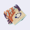 Folded fabric with a pattern of a fish and coral on a light blue background