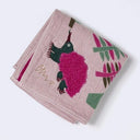 A folded light pink muslin cloth featuring a colorful embroidered design of an echidnas and tropical leaves, with a gold embroidered signature.