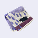 Folded towel with purple coloring of purple raindrops and a small hippo.