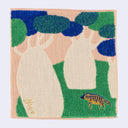 Square fabric towel with pink beige coloring and illustrated designs of large trunked trees and a grassy field with a small striped hyena.