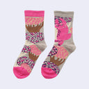 A pair of crew socks with a whimsical pattern featuring a pink cat, trees, and abstract shapes on a light gray background, with bright pink heels, toes, and cuffs.