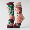 A pair of crew socks with a botanical and coral-like pattern in green, coral pink, and deep burgundy on a cream base, shown against a light gray studio background.