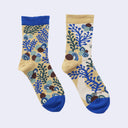 A pair of crew socks with a beige base featuring a blue, green, and brown coral-like botanical pattern, with solid blue cuffs, heels, and toes.