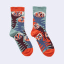 A pair of crew socks with a colorful abstract pattern featuring coral orange, sage green, slate blue, and dark plum, displayed against a light gray background.