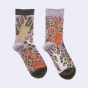A pair of crew socks with a complex botanical and tree pattern in orange, beige, white, and pink, set against a light gray background.