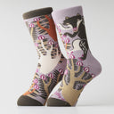 A pair of crew socks with a woodland animal pattern, featuring a black and white wolf among stylized trees on a light purple background.