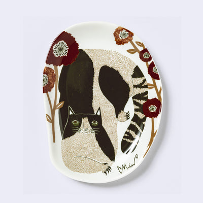 Decorative plate shaped like a slightly distorted oval with a cat design and floral elements, in muted tones of brown, orange and dark red. 