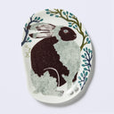 Decorative plate shaped like a slightly distorted oval with a crocodile design and floral elements, in muted tones of green, dark blue and purplish brown. 
