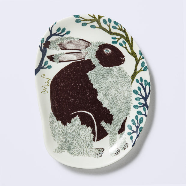 Decorative plate shaped like a slightly distorted oval with a crocodile design and floral elements, in muted tones of green, dark blue and purplish brown. 
