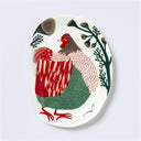 Decorative plate shaped like a slightly distorted oval with a rooster design and floral elements, in earthy tones of green and red. 