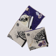 Rectangular textile with a pocket, the top can be folded over to make it into a pouch. Interior is purple and exterior is beige with designs of a purple bat, a tree and a moon. Shown both folded and with stored items within.