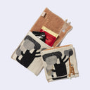 Rectangular textile with a pocket, the top can be folded over to make it into a pouch. Interior is orange and exterior is beige with designs of a gibbon hanging from a tree. Shown both folded over and holding items