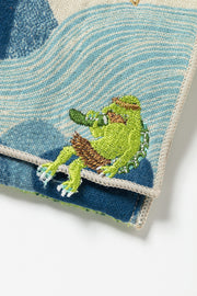 Embroidered green kappa character. eating a cucumber on a textured blue and white fabric