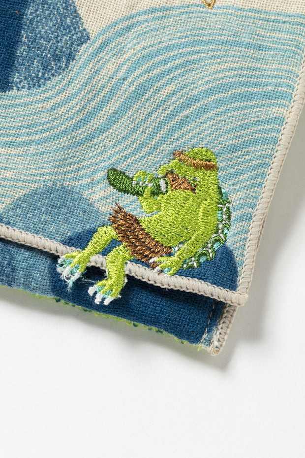 Embroidered green kappa character. eating a cucumber on a textured blue and white fabric