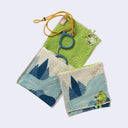 Rectangular textile with a pocket, the top can be folded over to make it into a pouch. Interior is bright green and exterior is beige with designs of a kappa sitting on rocks near a river. Shown both folded over and holding items within in.