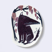 Decorative plate shaped like a slightly distorted oval with a wolf design and floral elements, in muted tones of dark blue, dark purple and dark orange/red.