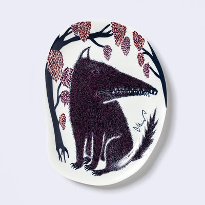 Decorative plate shaped like a slightly distorted oval with a wolf design and floral elements, in muted tones of dark blue, dark purple and dark orange/red.