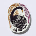 Decorative plate shaped like a slightly distorted oval with a goose design and floral elements, in muted tones of mint black, orange and purple. It has 2 baby goslings on its back. 