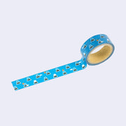 Roll of blue washi tape with illustrations of a simple, geometric Mt. Fuji, dark blue with snow capped top. Randomly in the pattern are small clouds or a small red sun.