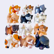 12 different small cat figurines, all sitting and licking their underside. Colorways vary.