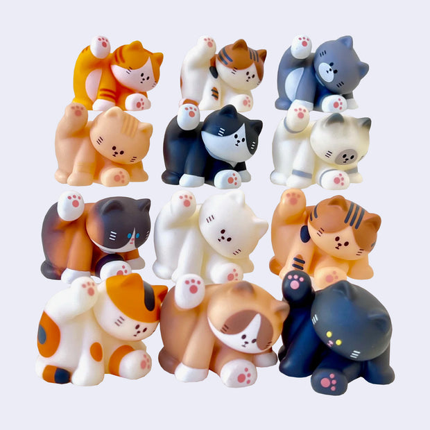 12 different small cat figurines, all sitting and licking their underside. Colorways vary.