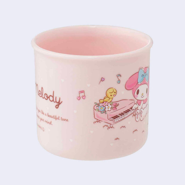 Short pink cup with a mug handle featuring a vintage style illustration of Sanrio's My Melody, sitting and playing a small piano. She is surrounded by cute, small animals such as a mouse, squirrel and bird.